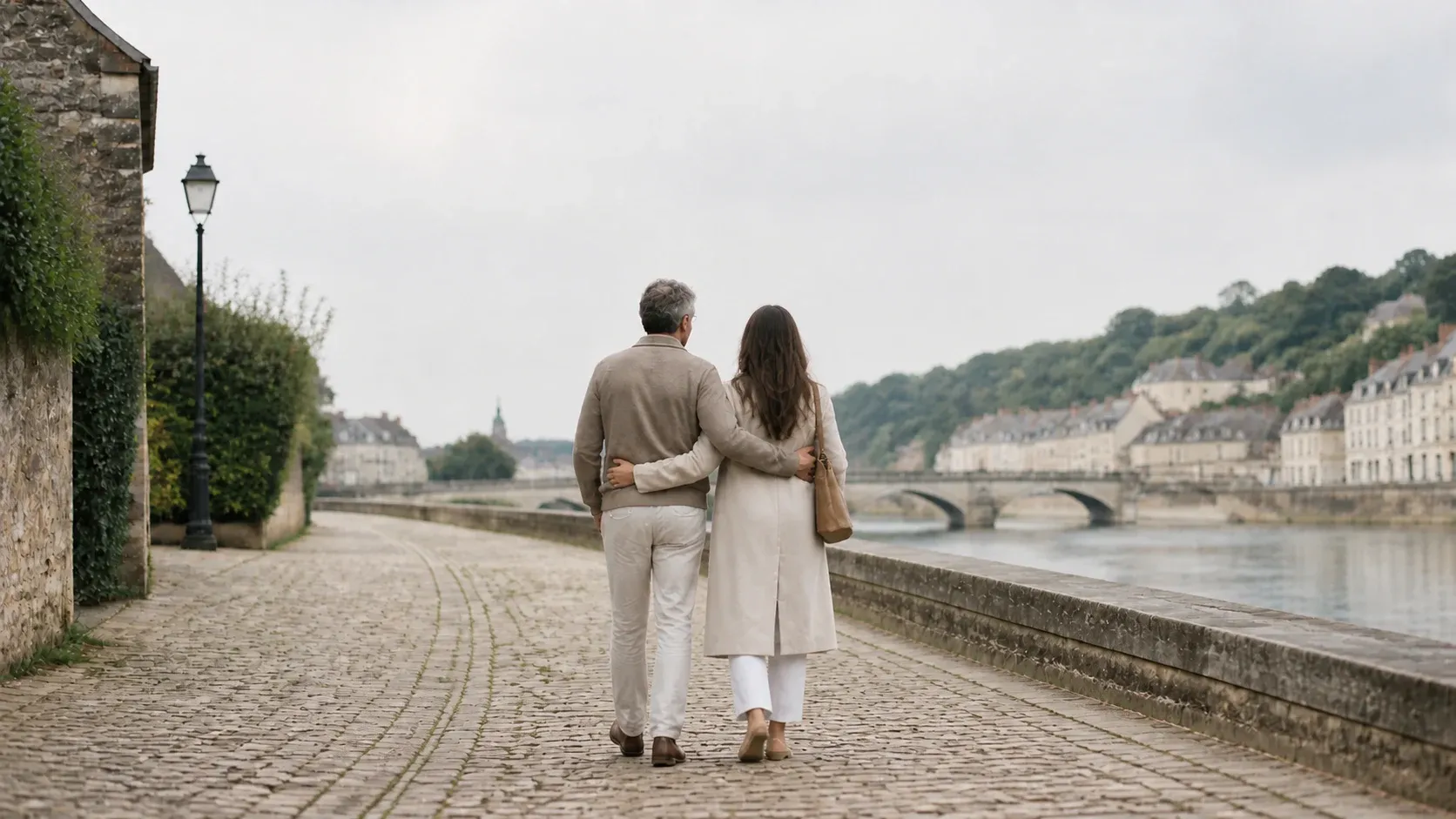 A couple walking close together beside a European riverside in the morning